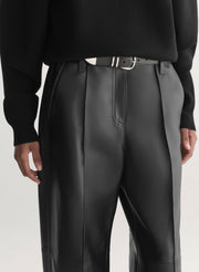 Person wearing a black turtleneck and black leather pants on a light gray background