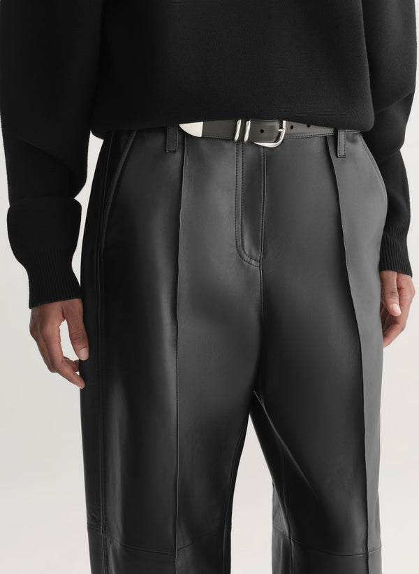 Person wearing a black turtleneck and black leather pants on a light gray background