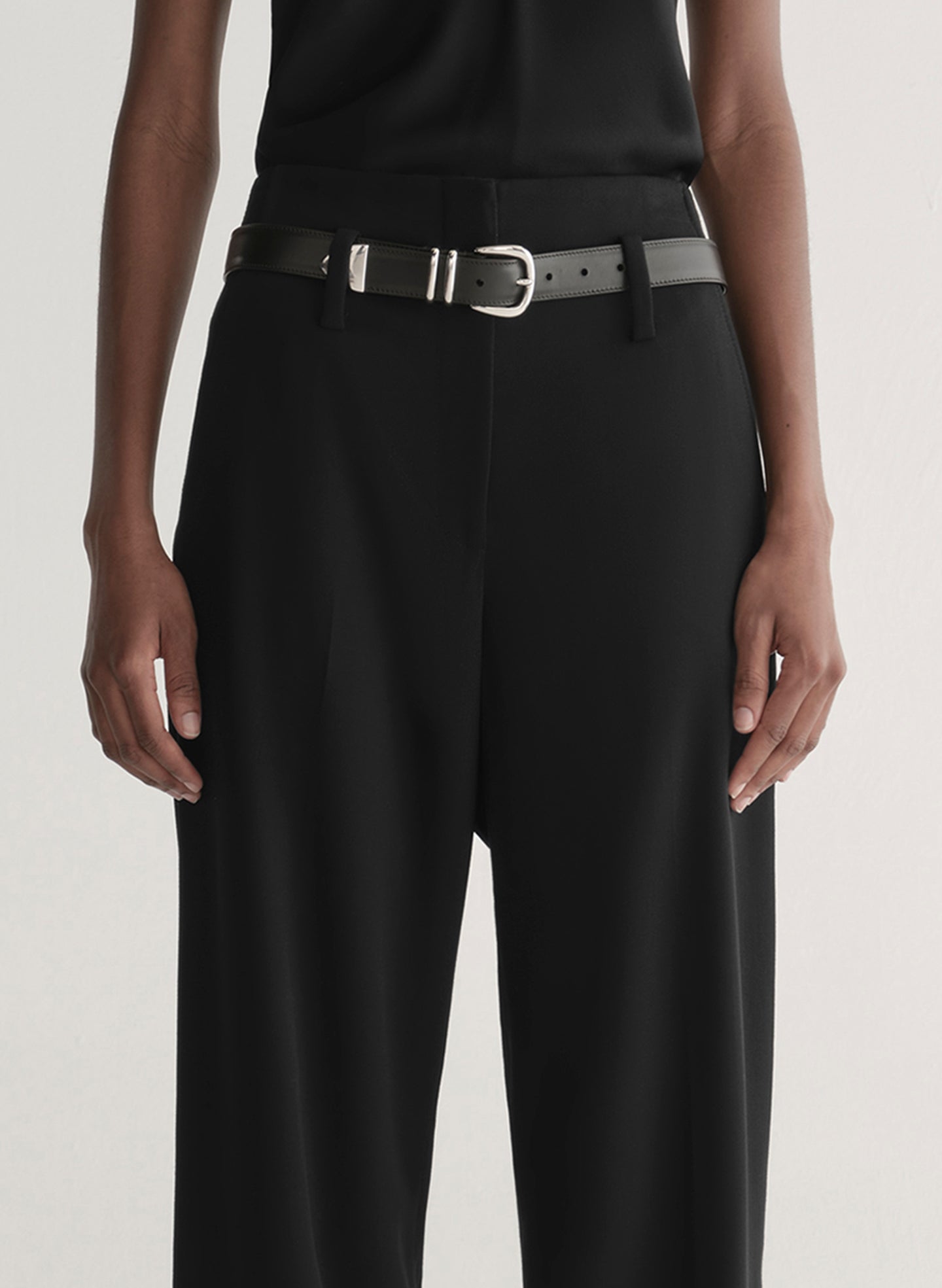 Person wearing a black sleeveless top and wide-leg pants on a white 