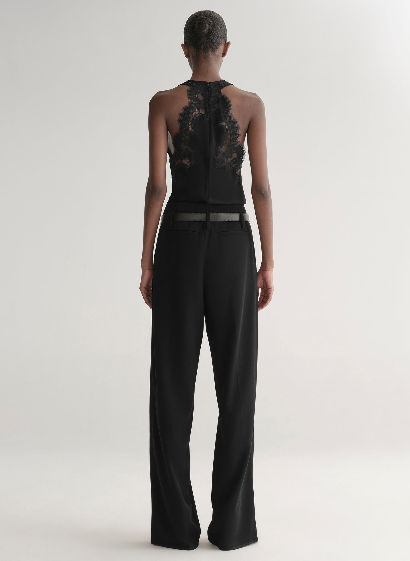 Person wearing a black sleeveless top with lace detailing and high-waisted black pants on a white background