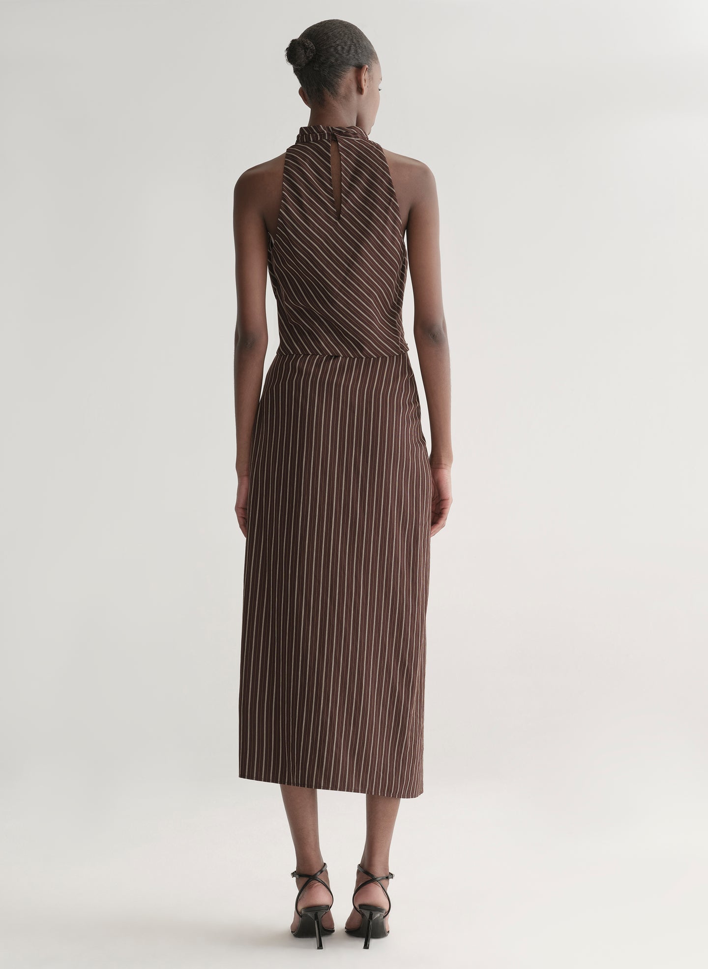 Woman wearing a brown striped top and matching midi skirt against a plain background