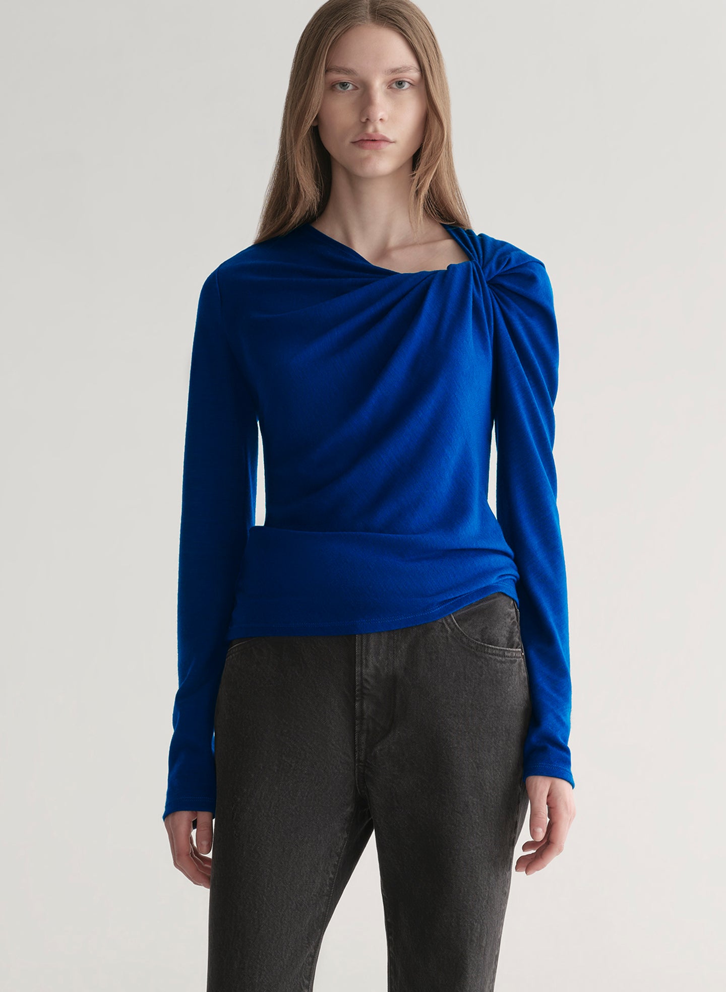 woman wearing a blue long-sleeve top with a draped design on a plain background