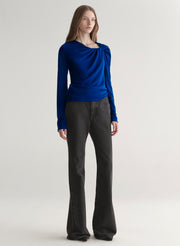 woman wearing a blue long-sleeve top with a draped design on a plain background