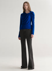 woman wearing a blue long-sleeve top with a draped design on a plain background