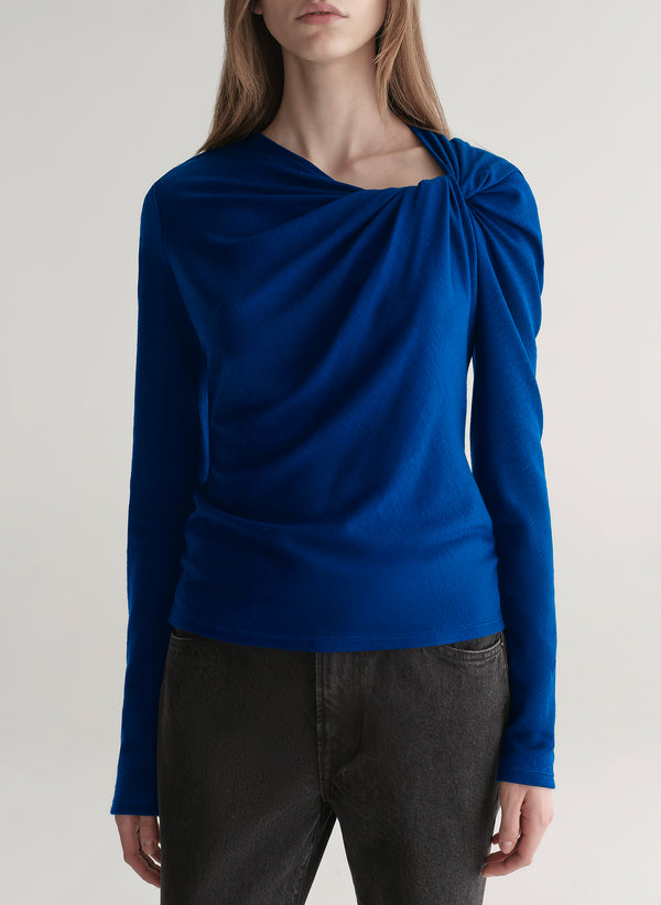 woman wearing a blue long-sleeve top with a draped design on a plain background