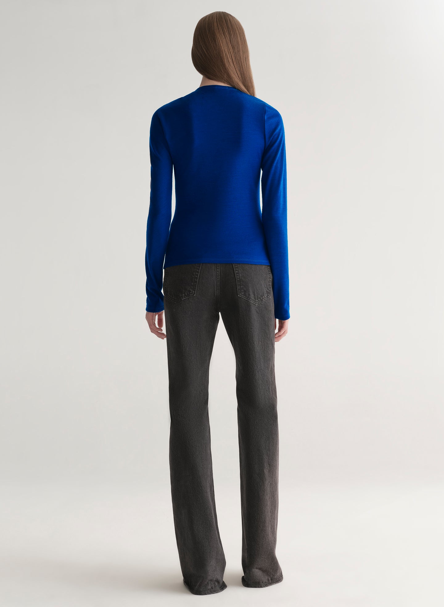 woman wearing a blue long-sleeve top with a draped design on a plain background