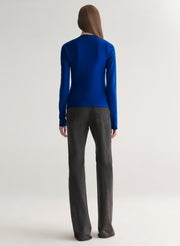 woman wearing a blue long-sleeve top with a draped design on a plain background