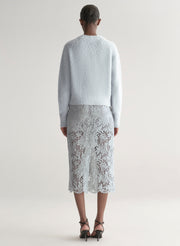 Person wearing a light blue sweater and lace skirt on a plain background