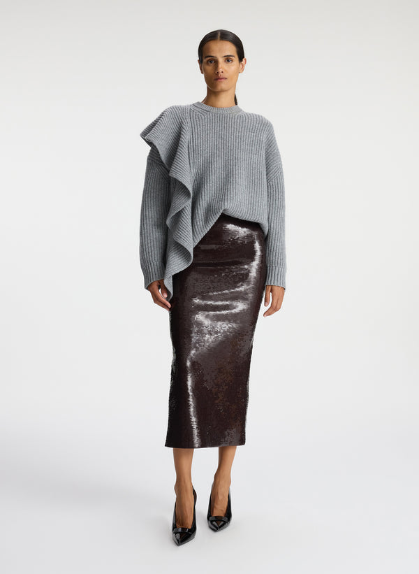front view of woman wearing grey sweater with ruffle and brown sequin midi skirt