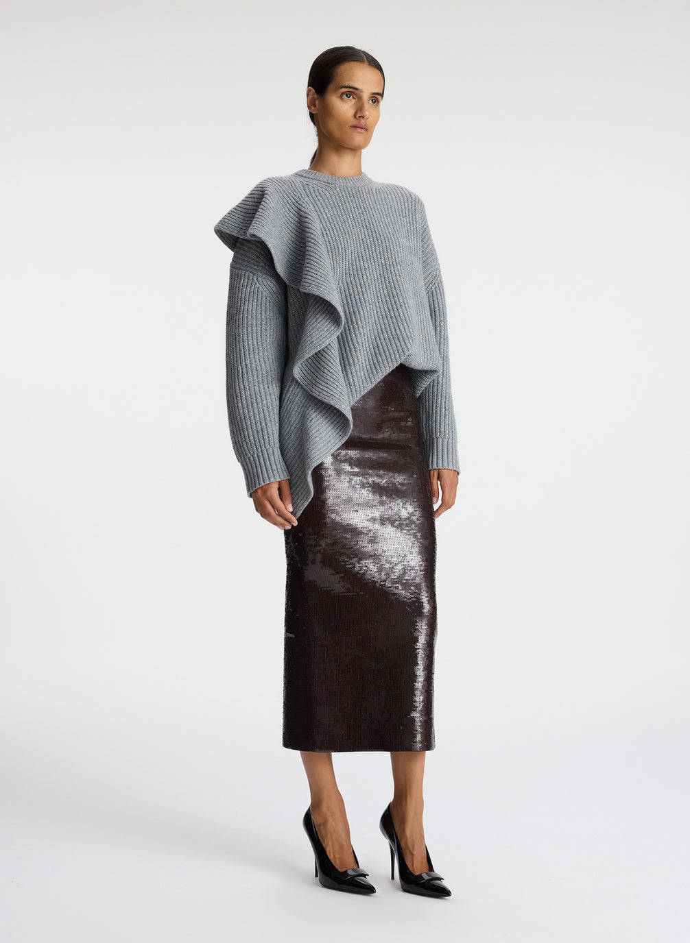 side view of woman wearing grey sweater with ruffle and brown sequin midi skirt