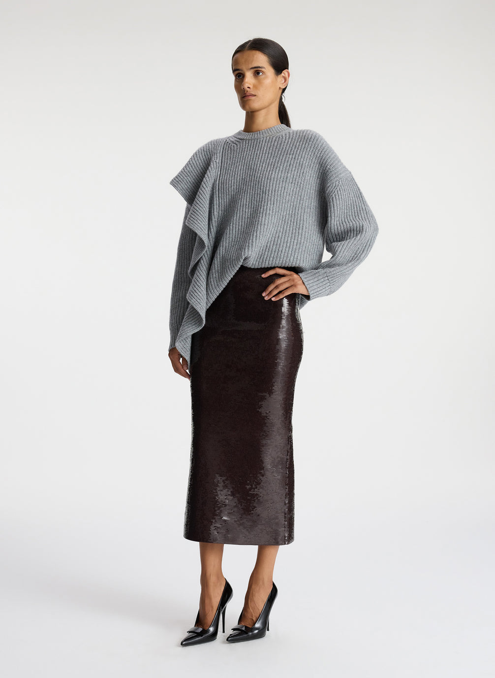 side view of woman wearing grey sweater with ruffle and brown sequin midi skirt