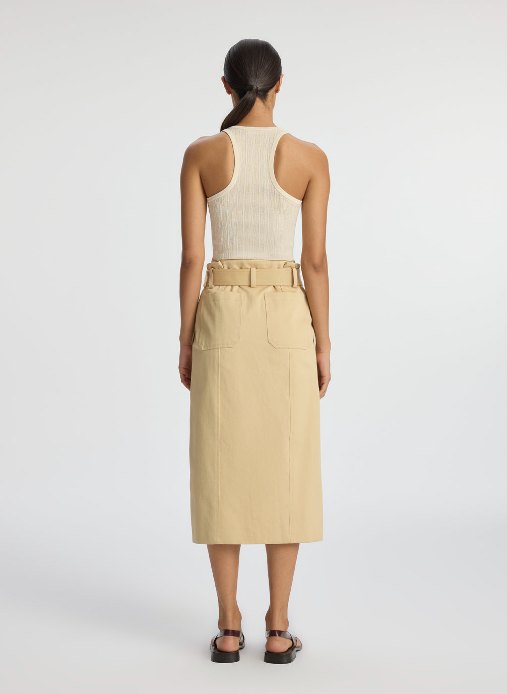 back view of woman wearing beige tank top and tan midi skirt