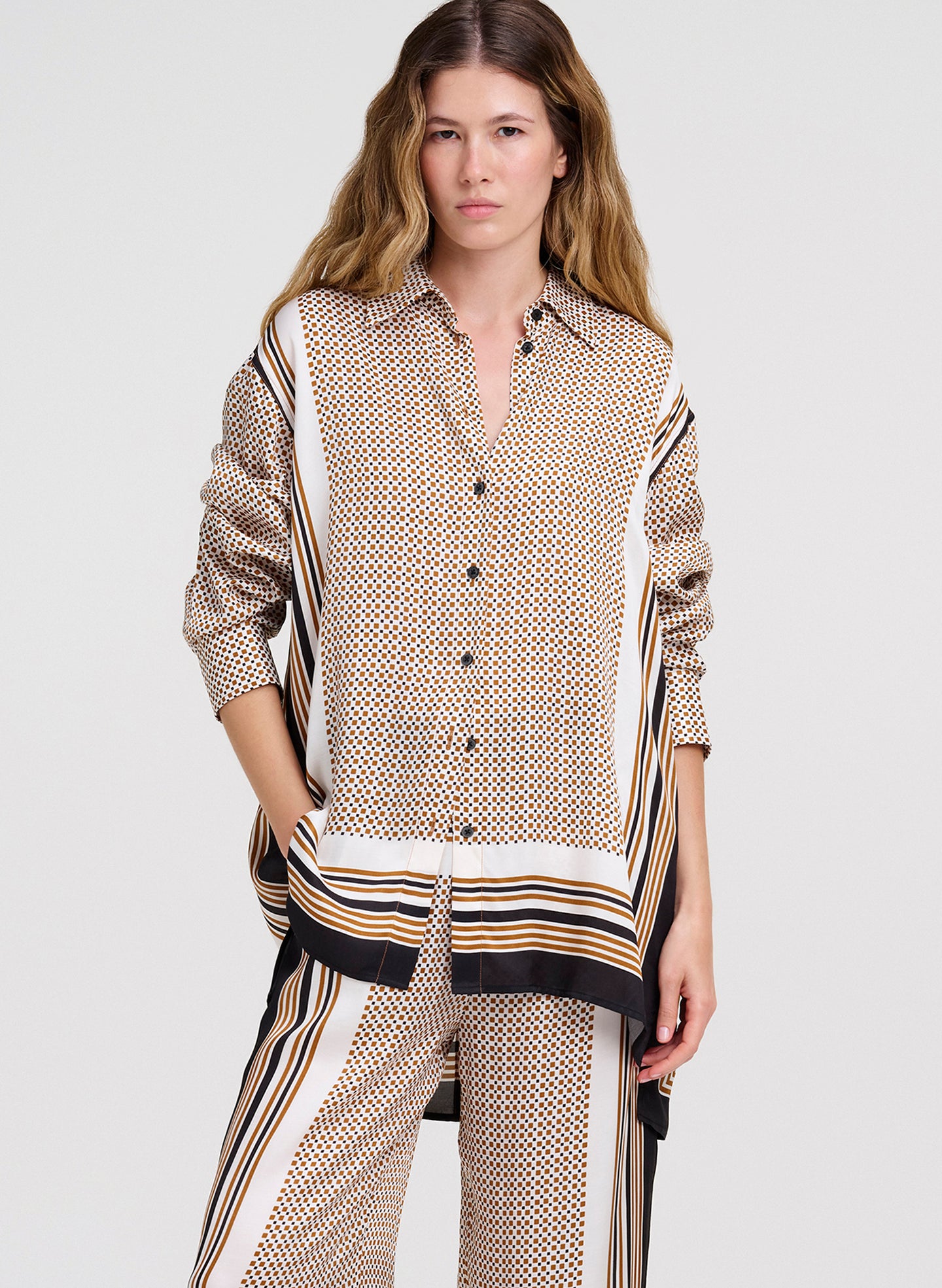 Woman wearing a patterned shirt and pants on a plain background
