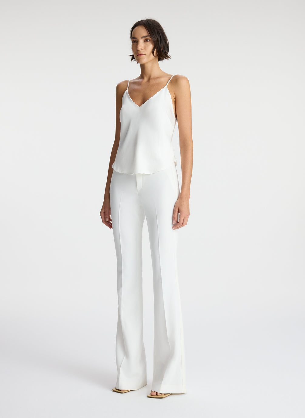 side view of woman wearing white satin camisole and white pants