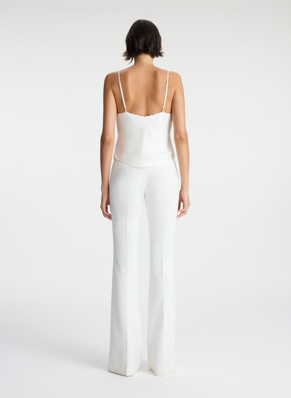 back view of woman wearing white satin camisole and white pants
