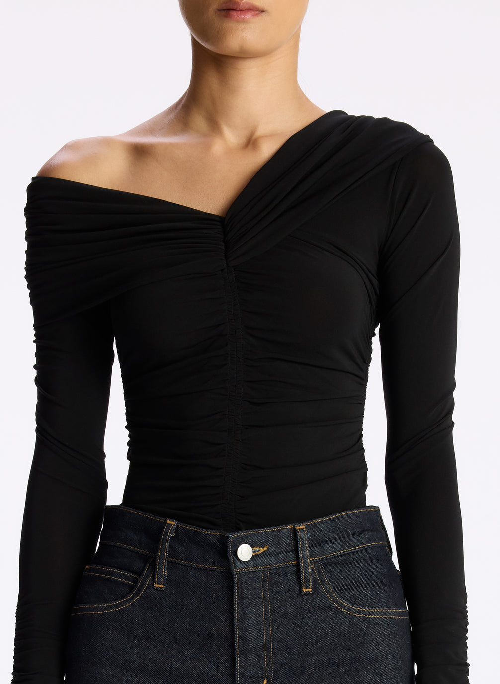 detail view of woman wearing black off shoulder long sleeve jersey top and dark wash denim jeans