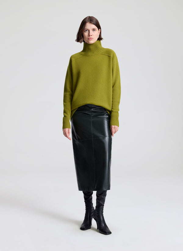 Woman wearing a green sweater and dark green leather skirt on a white background
