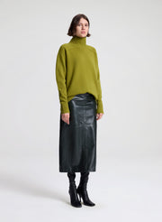 Woman wearing a green sweater and dark green leather skirt on a white background