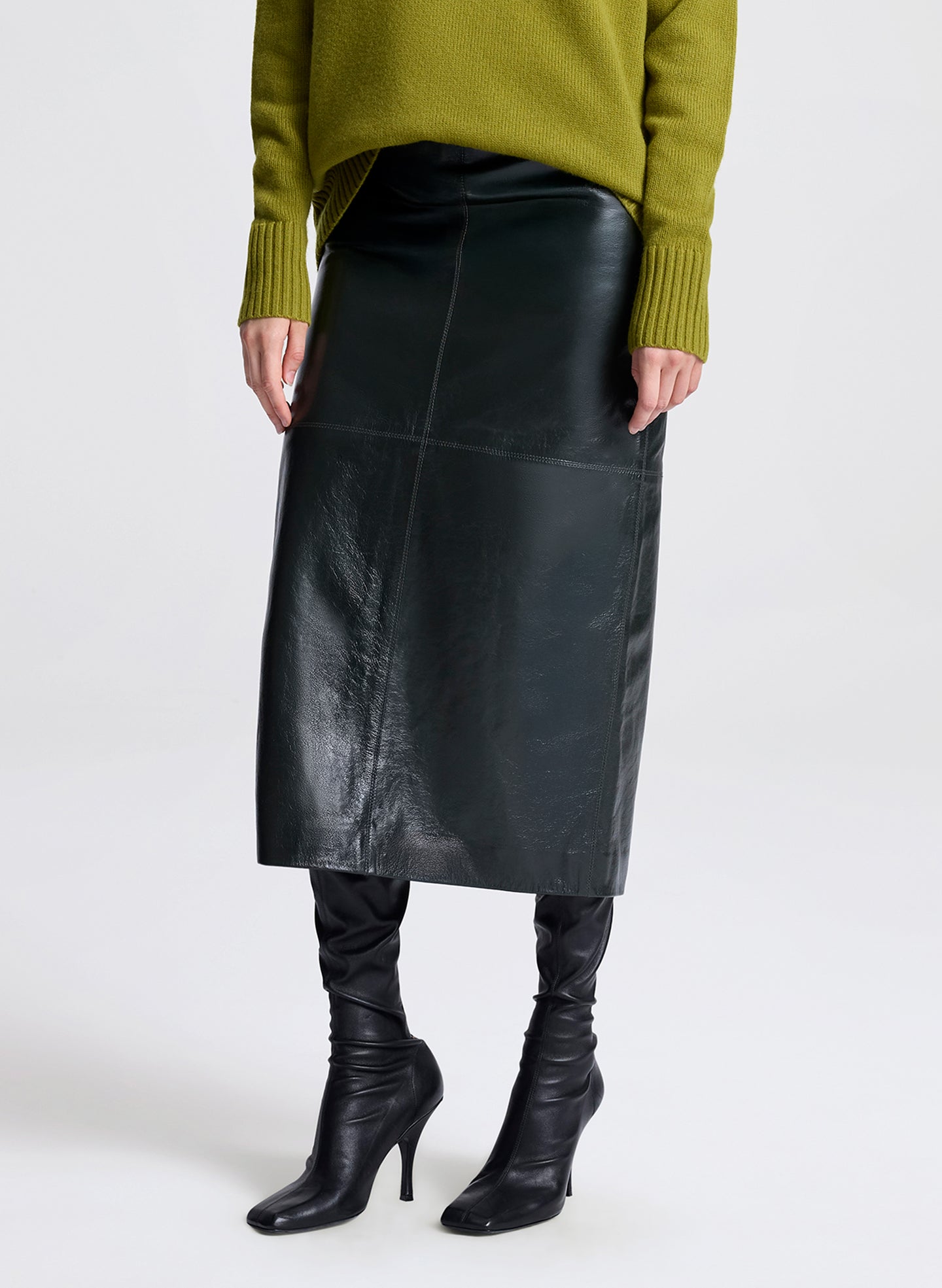 Woman wearing a green sweater and dark green leather skirt on a white background