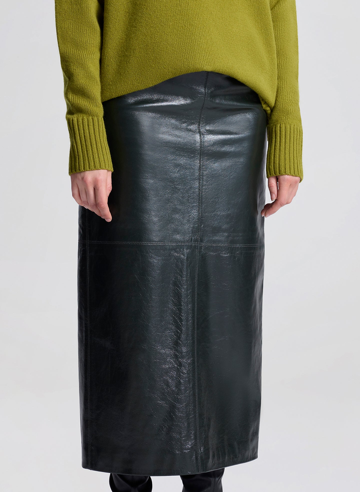 Woman wearing a green sweater and dark green leather skirt on a white background