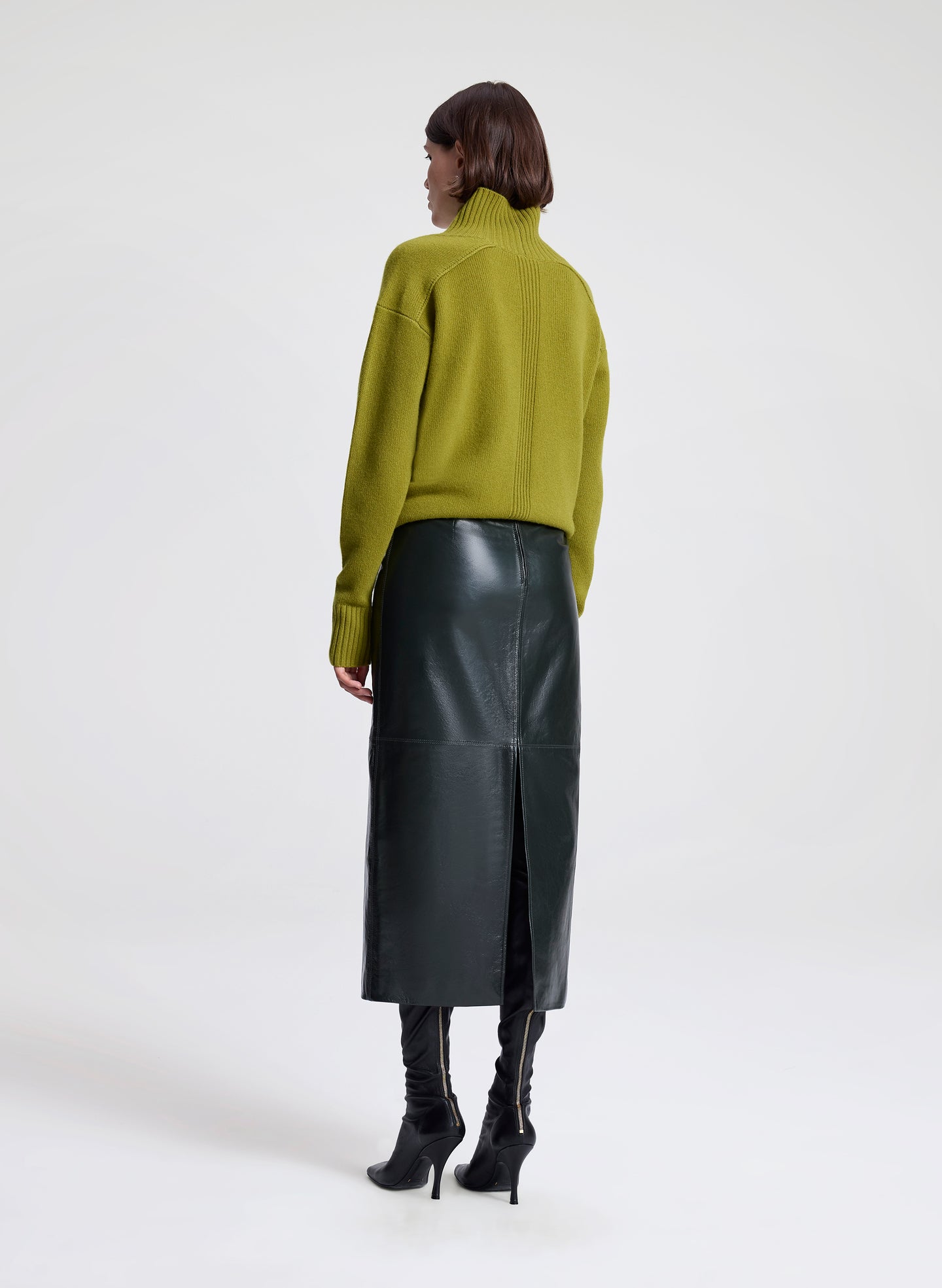 Woman wearing a green sweater and dark green leather skirt on a white background
