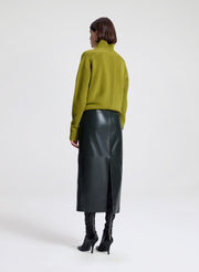 Woman wearing a green sweater and dark green leather skirt on a white background
