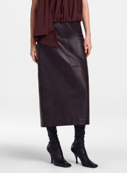 A model is shown from the waist down wearing a dark brown leather midi skirt, a matching brown draped top, and black heeled ankle boots against a light gray studio background.