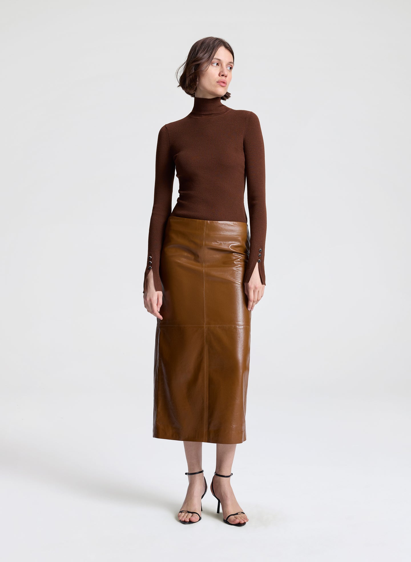 Woman wearing a brown turtleneck and leather skirt on a white background