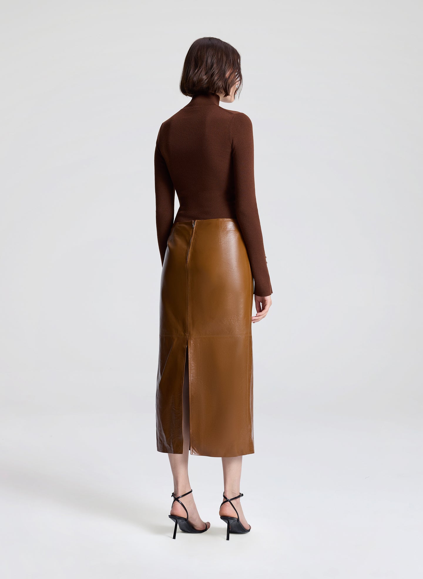 Person wearing a brown leather skirt and brown top on a white background