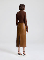 Person wearing a brown leather skirt and brown top on a white background