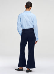 A model shown from the back wearing a light blue long-sleeve button-down shirt and dark navy flared trousers, paired with dark loafers, against a light gray studio background.