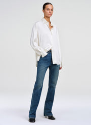 A model wearing a white long-sleeve button-down shirt and blue jeans, standing against a light gray studio background.