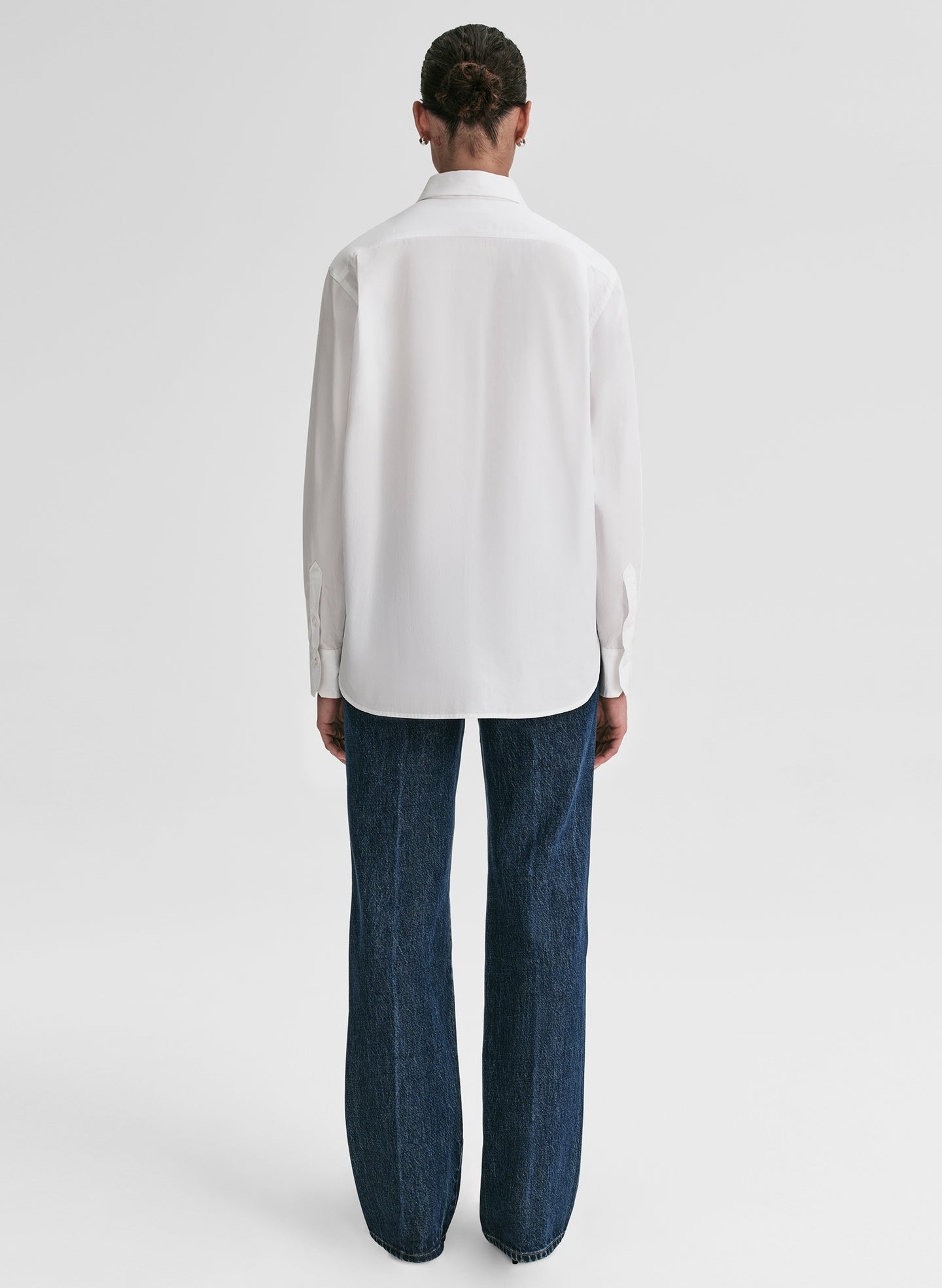 Person wearing a white shirt and dark jeans on a light gray background