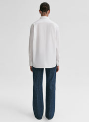 Person wearing a white shirt and dark jeans on a light gray background