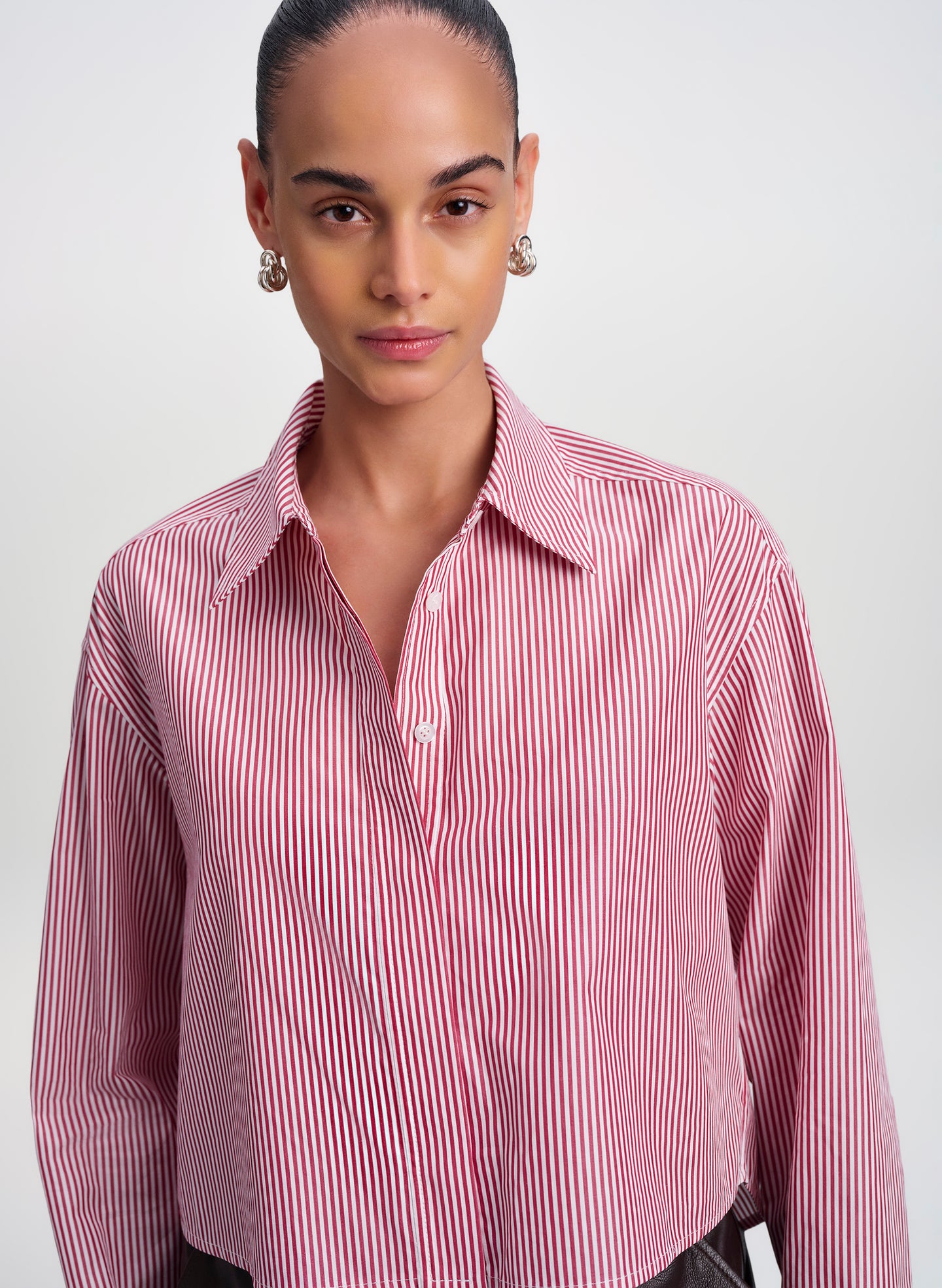 A model wearing a red and white vertically striped button-down shirt, photographed against a neutral light gray studio background.