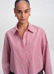 A model wearing a red and white vertically striped button-down shirt, photographed against a neutral light gray studio background.