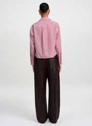 A model viewed from the back wearing a striped red and white long-sleeve button-up shirt and dark brown wide-leg trousers, set against a plain light gray studio background.