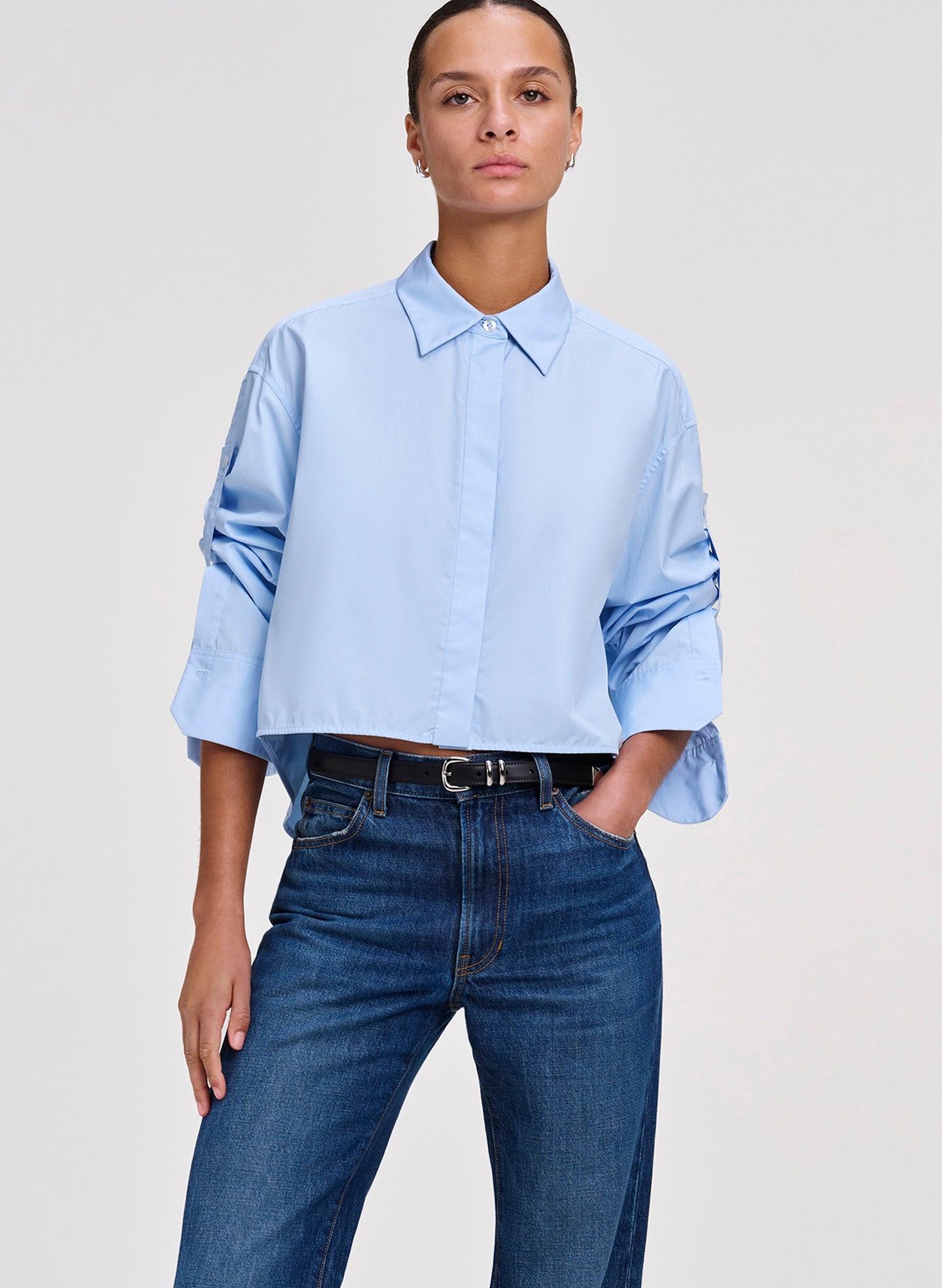 Person wearing a light blue shirt and blue jeans on a plain background