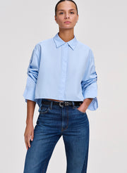 Person wearing a light blue shirt and blue jeans on a plain background