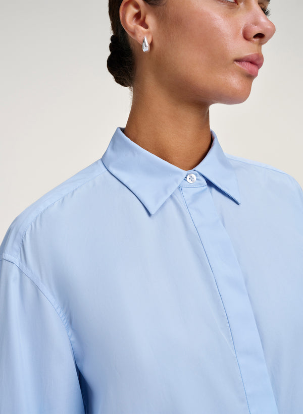 Person wearing a light blue shirt with a neutral background
