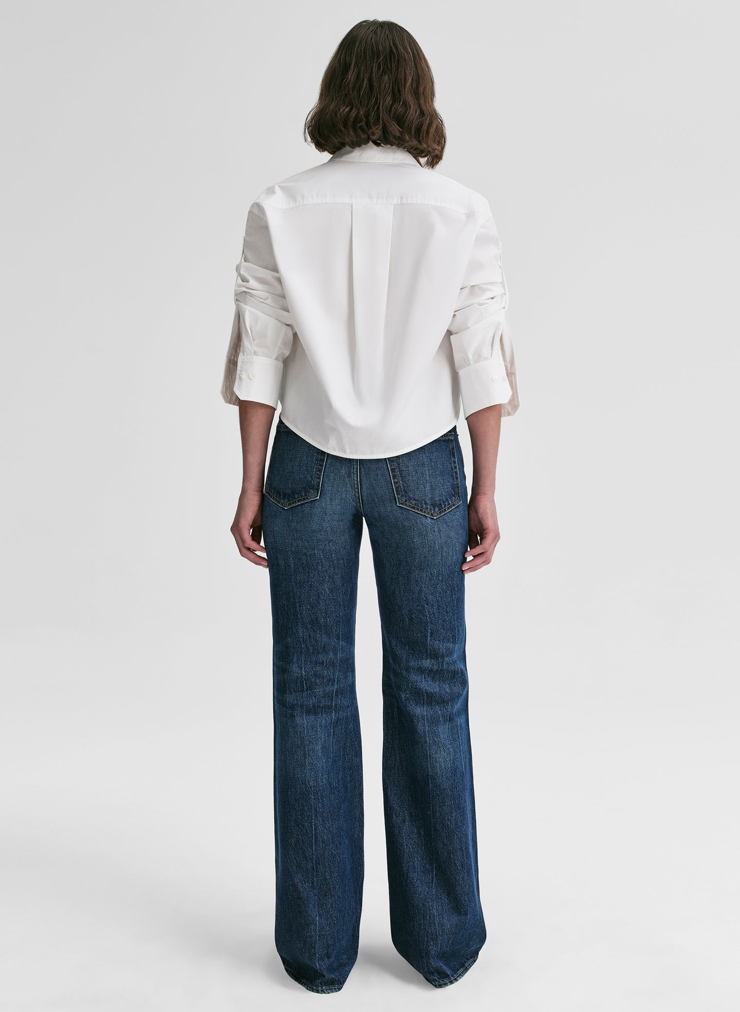 Person wearing a white shirt and blue jeans on a plain background