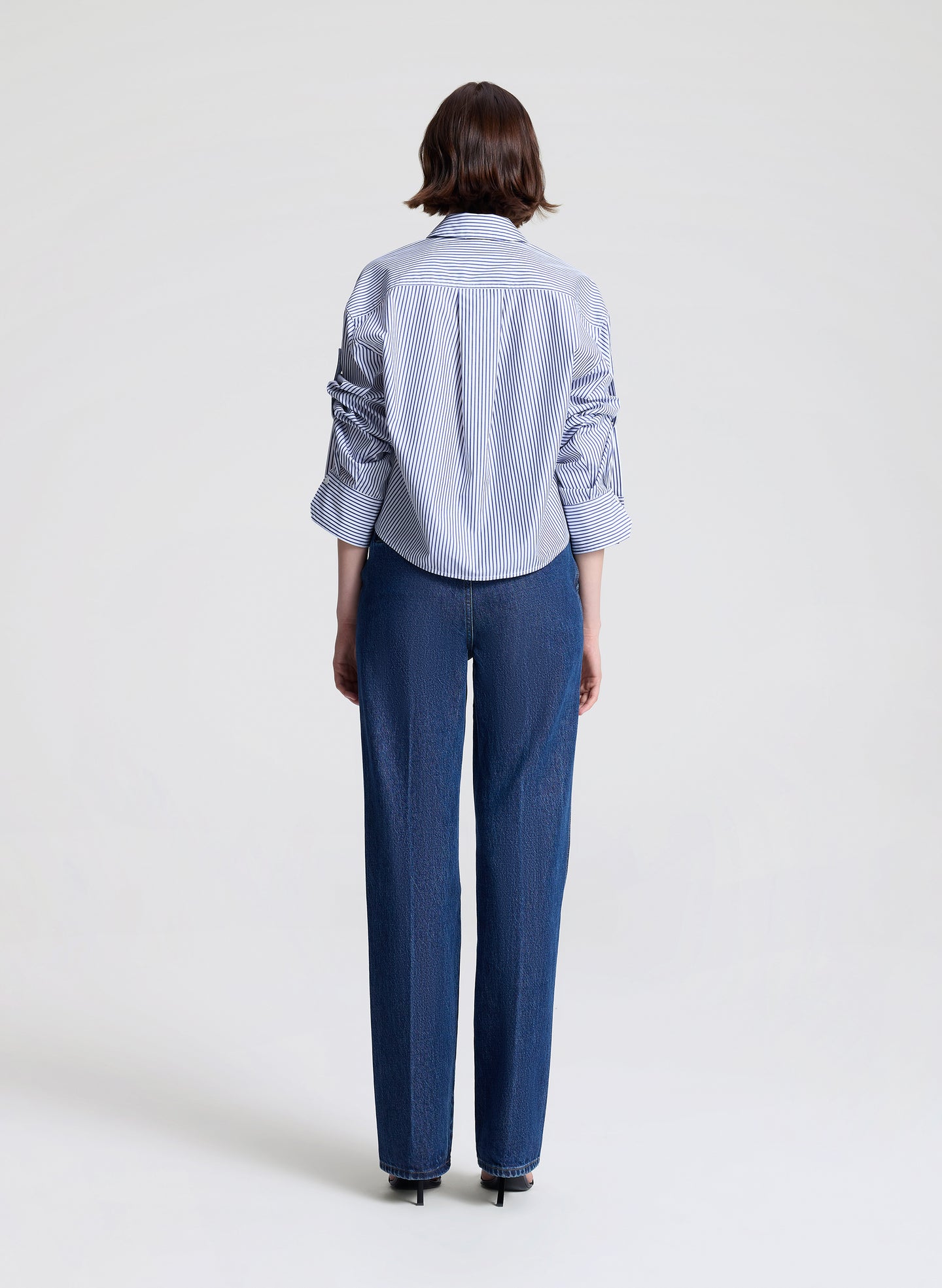 Person wearing a striped shirt and blue jeans on a light gray background