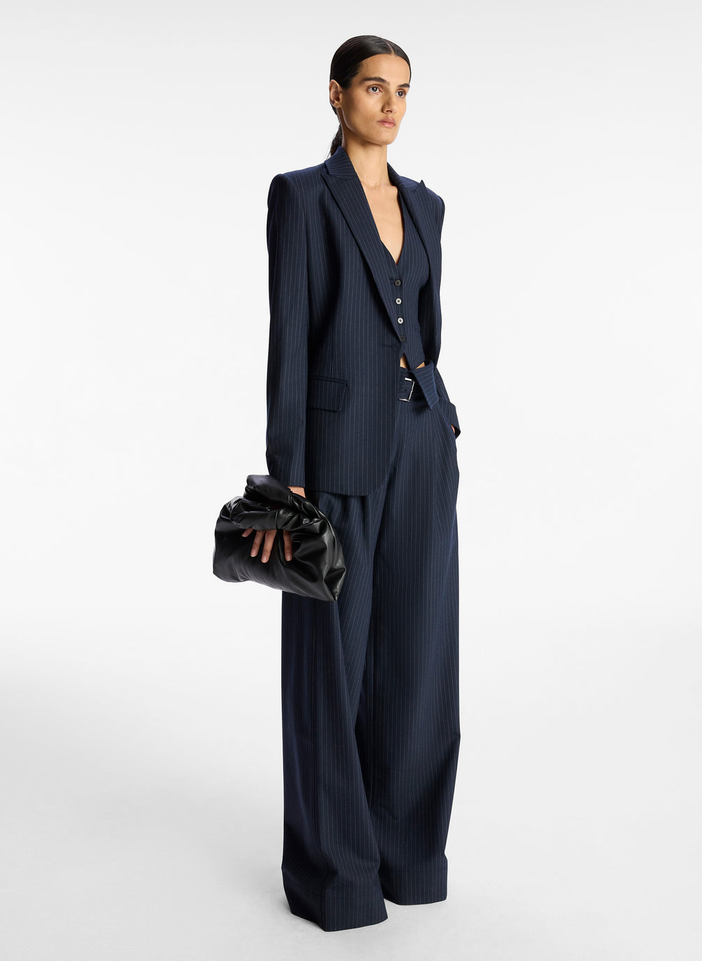 side  view of woman wearing navy blue pinstripe suit comprised of blazer, vest, and fold over wide leg pants