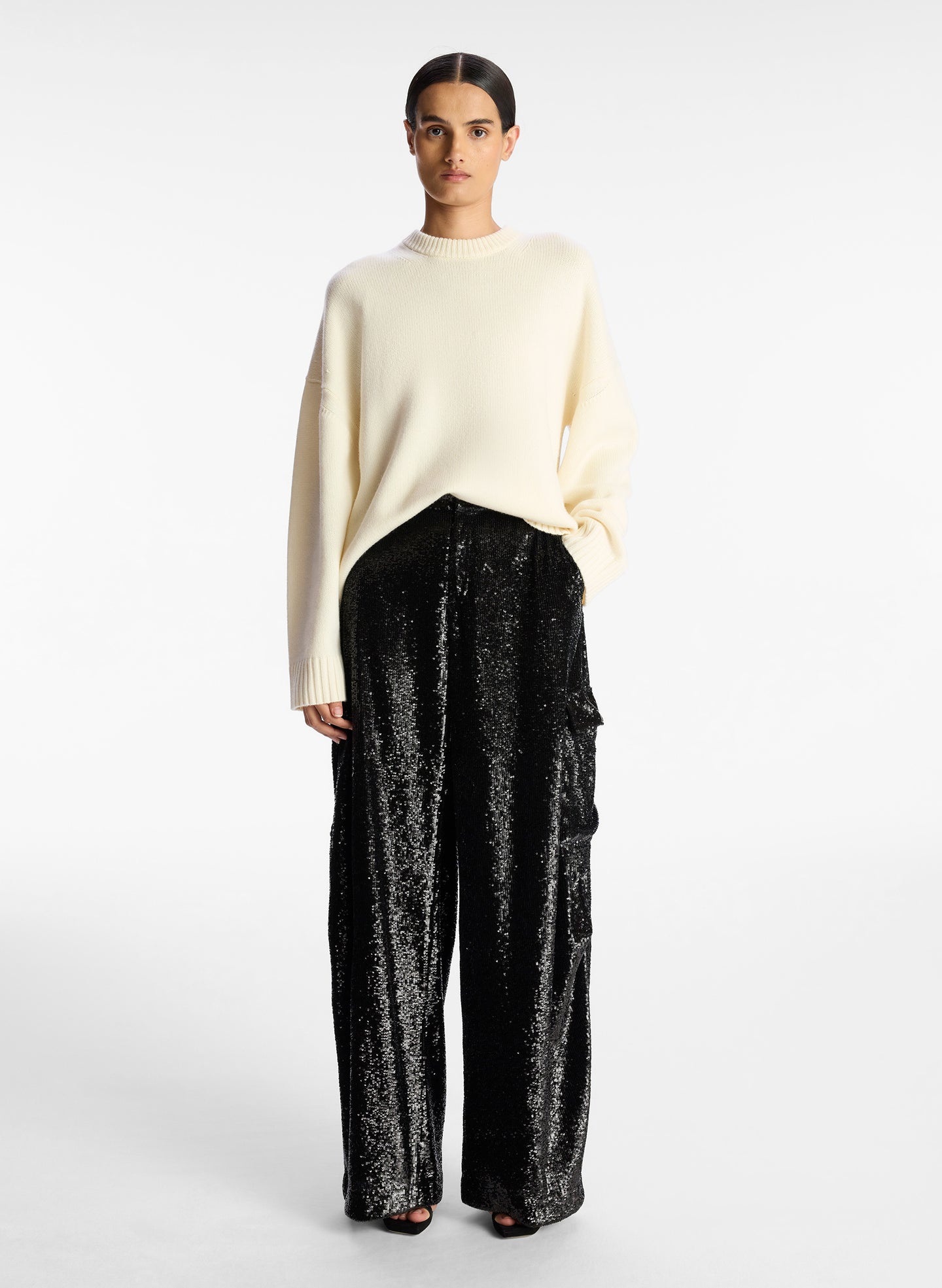 front view of woman wearing cream sweater and black sequined cargo pants