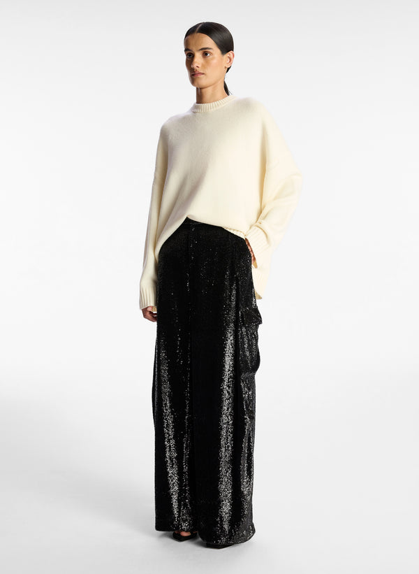 side view of woman wearing cream sweater and black sequined cargo pants