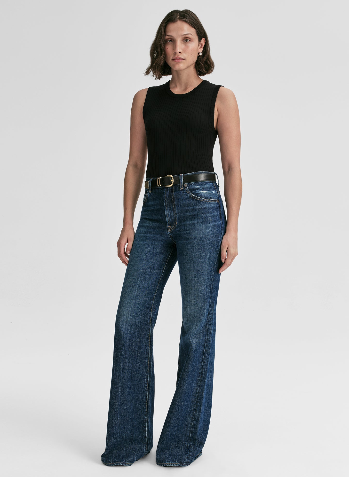 Woman wearing a black sleeveless top and blue jeans on a white background