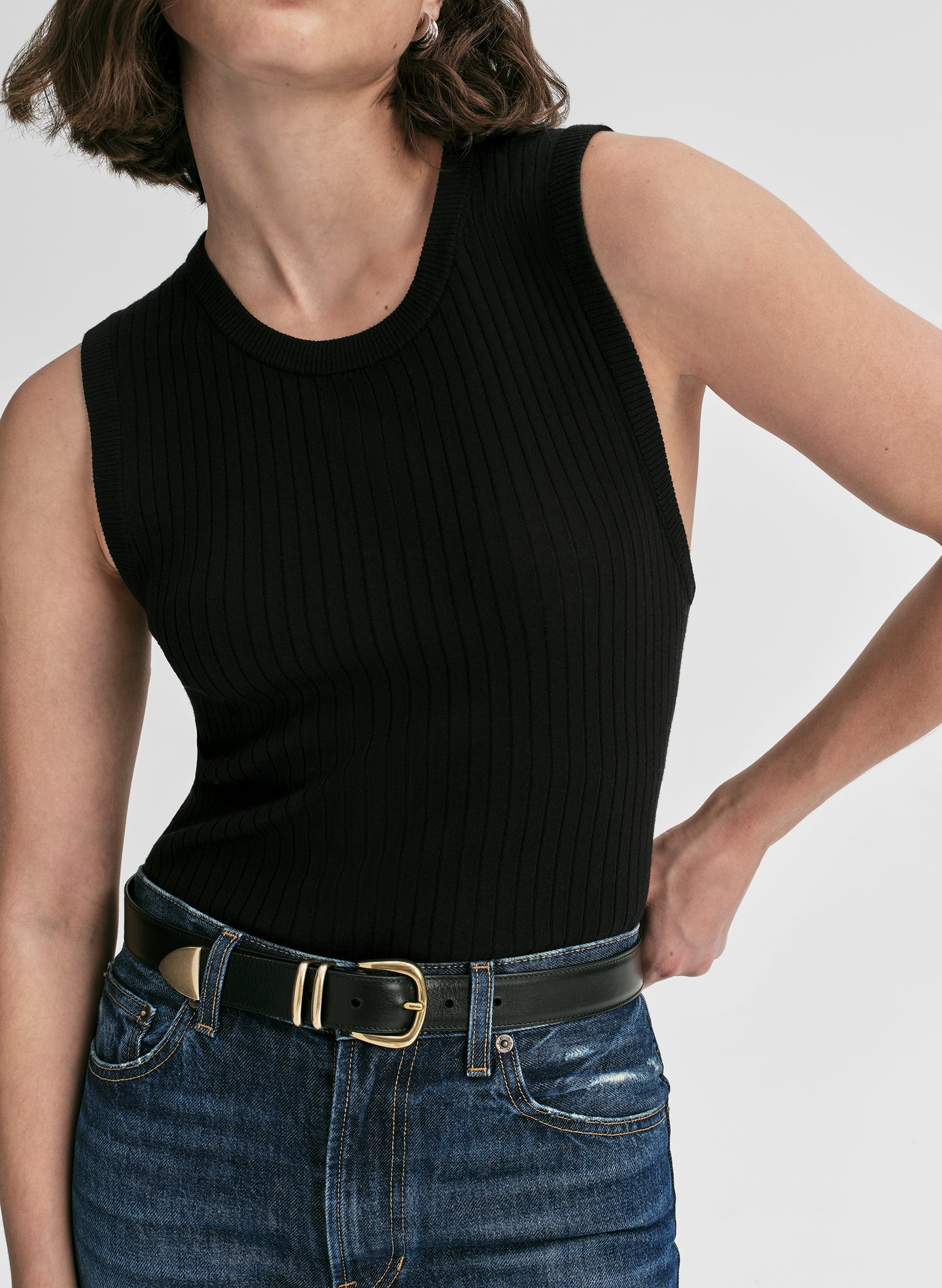 Person wearing a black sleeveless top and blue jeans on a plain background