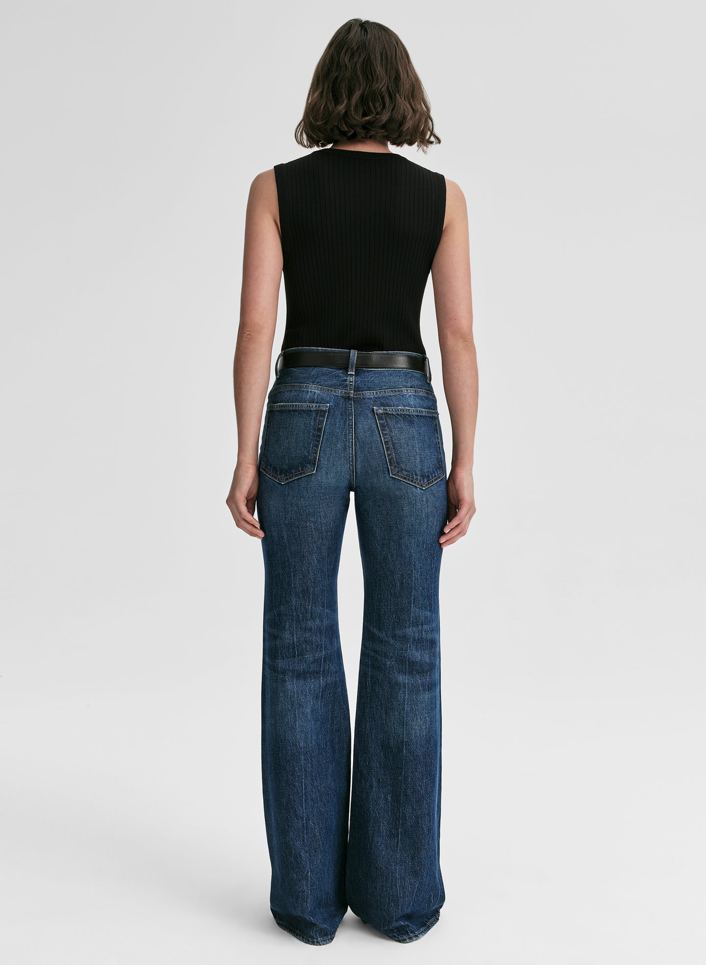 Person wearing blue jeans and a black sleeveless top on a white background