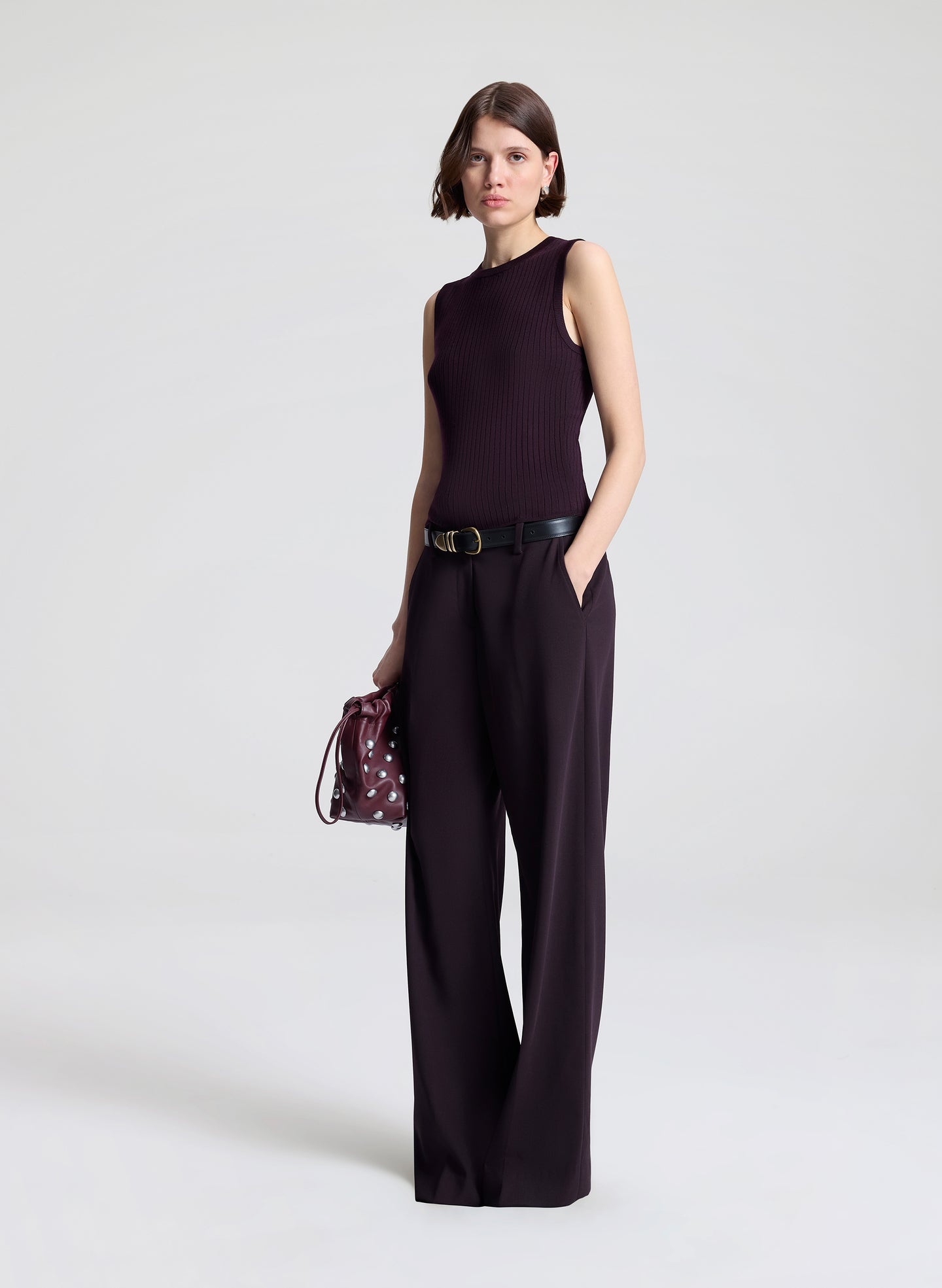 Woman wearing a purple sleeveless top and purple pants, holding a matching handbag against a light background