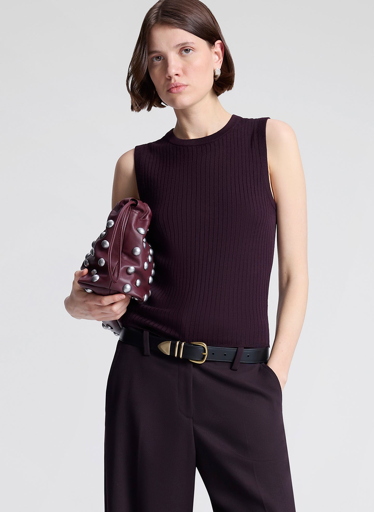 Woman wearing a purple sleeveless top and purple pants, holding a matching handbag against a light background